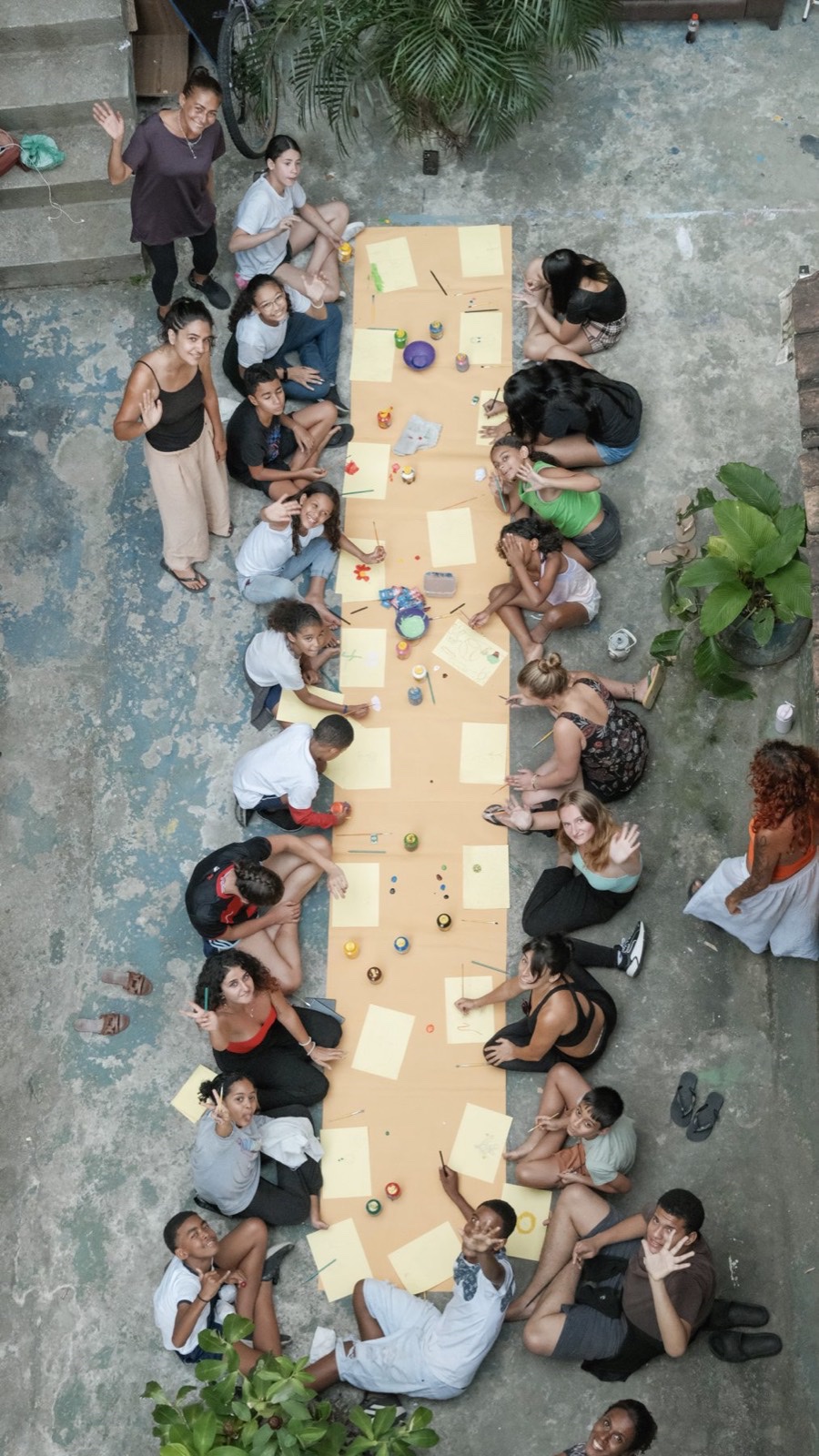 Seen from above, children and volunteers paint on a long strip of paper laid along a Vidigal street.
