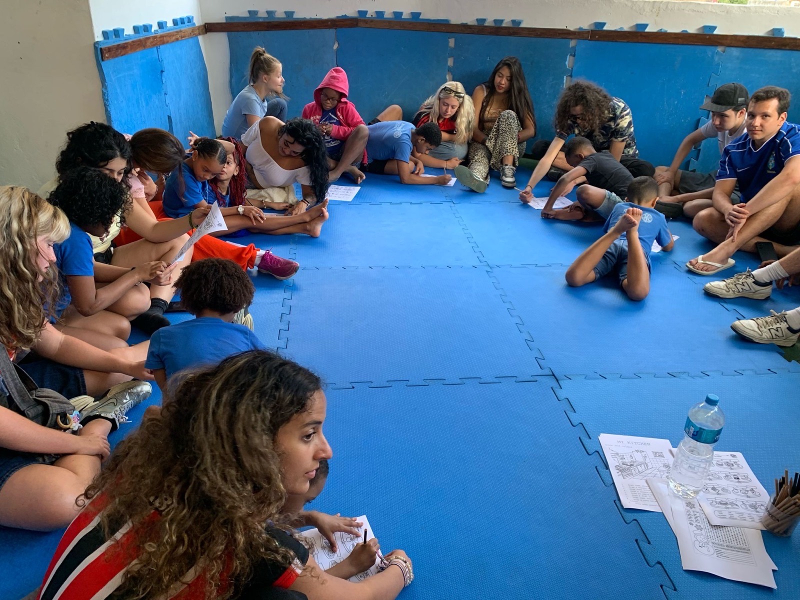 Young people and volunteers sit together in a circle on blue mats, talking during a workshop.