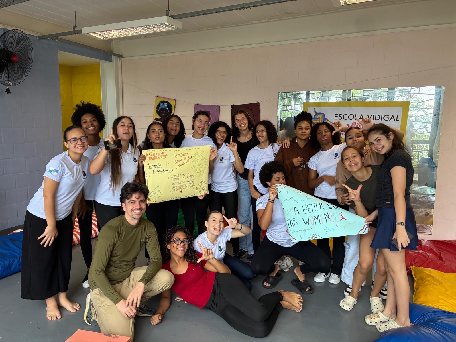 Students and our volunteers pose together in a classroom at Escola Vidigal, holding up handmade signs.