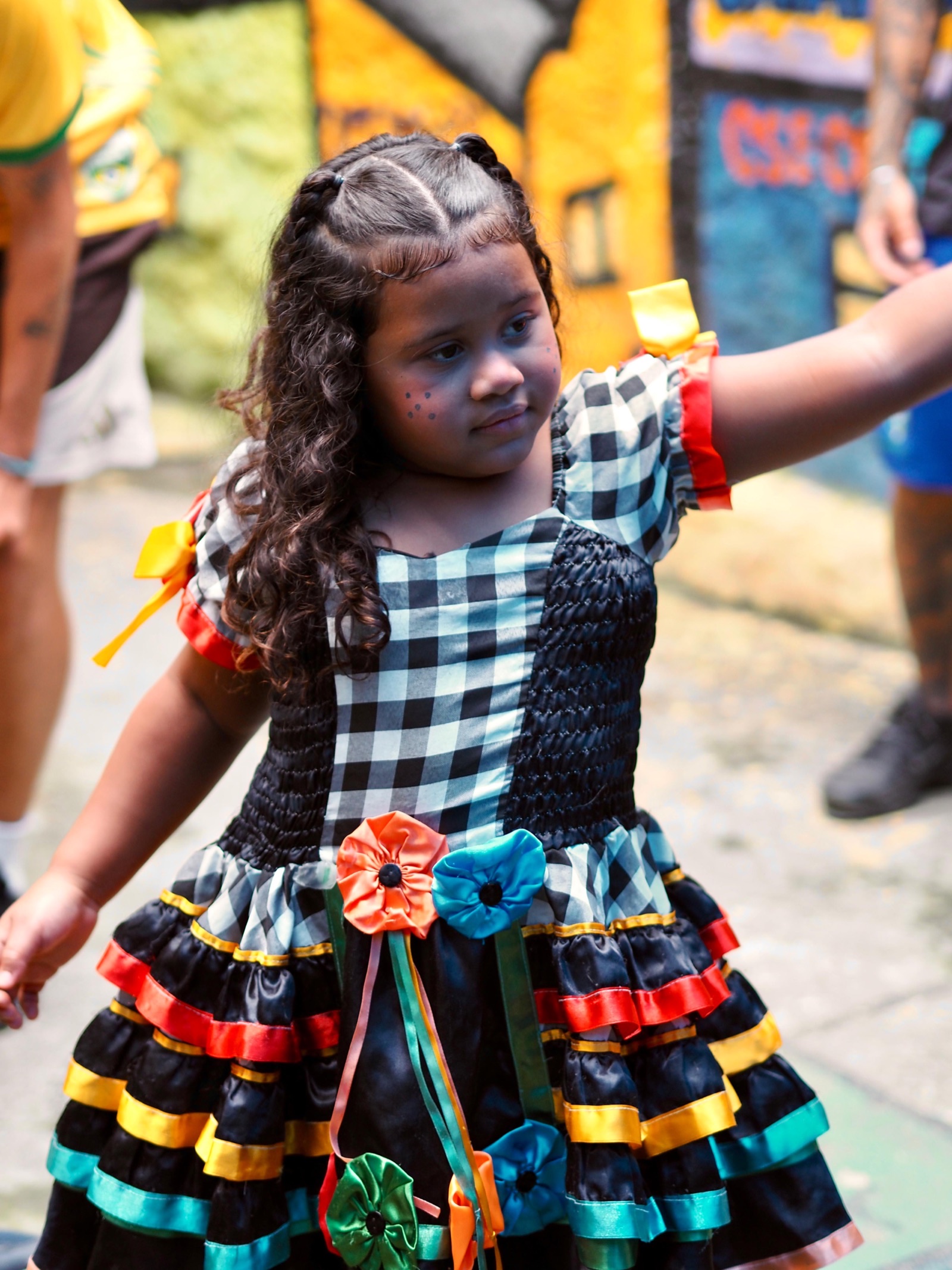 A young girl in a checked, ruffled dress dances with her arms out.