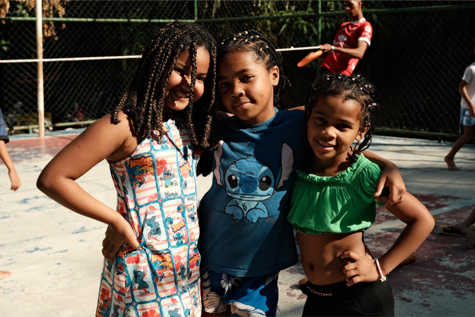Three girls with their arms around each other smile at the camera on the sports court.