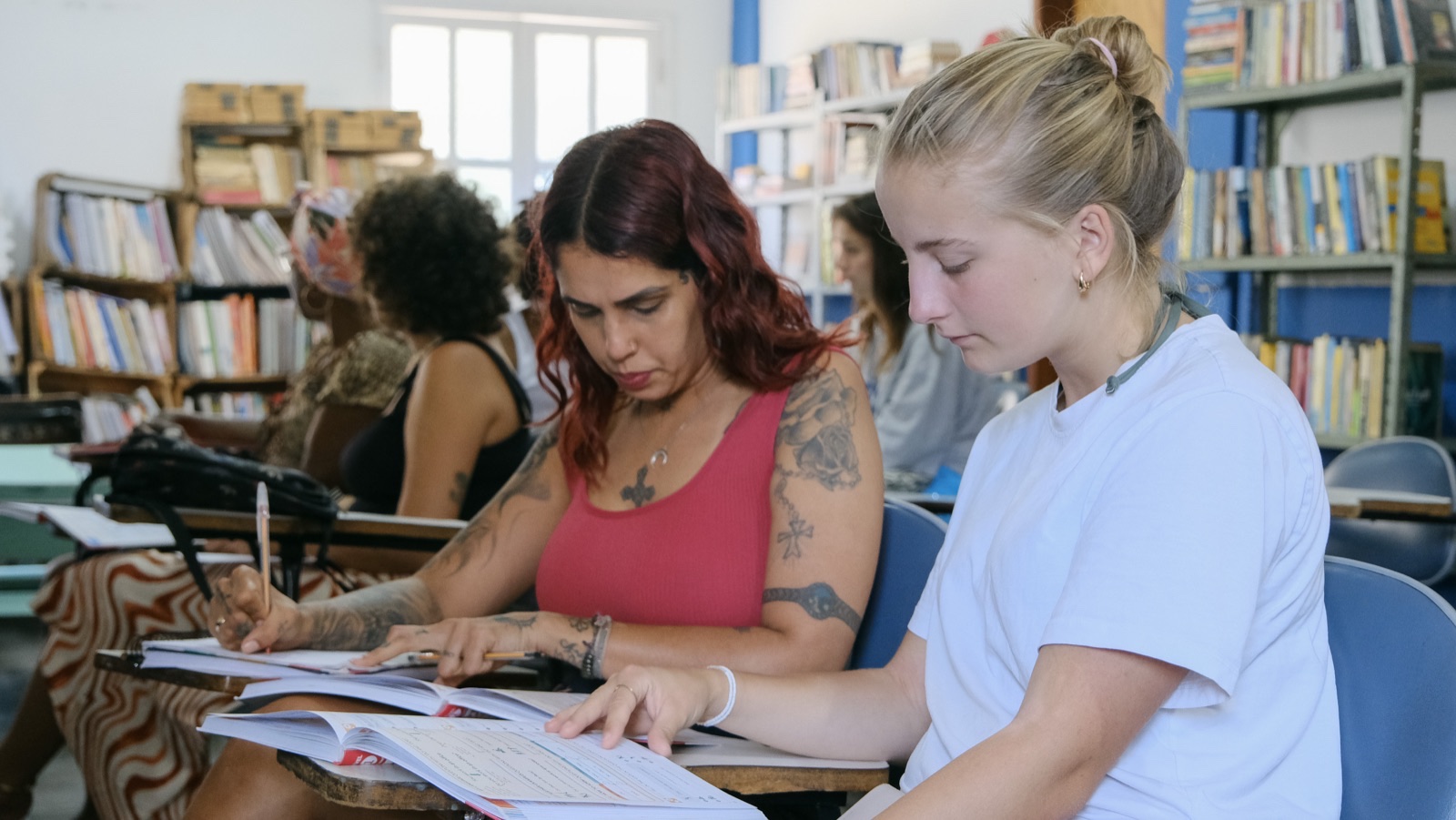 Two volunteers read through English worksheets together at a table in a library.