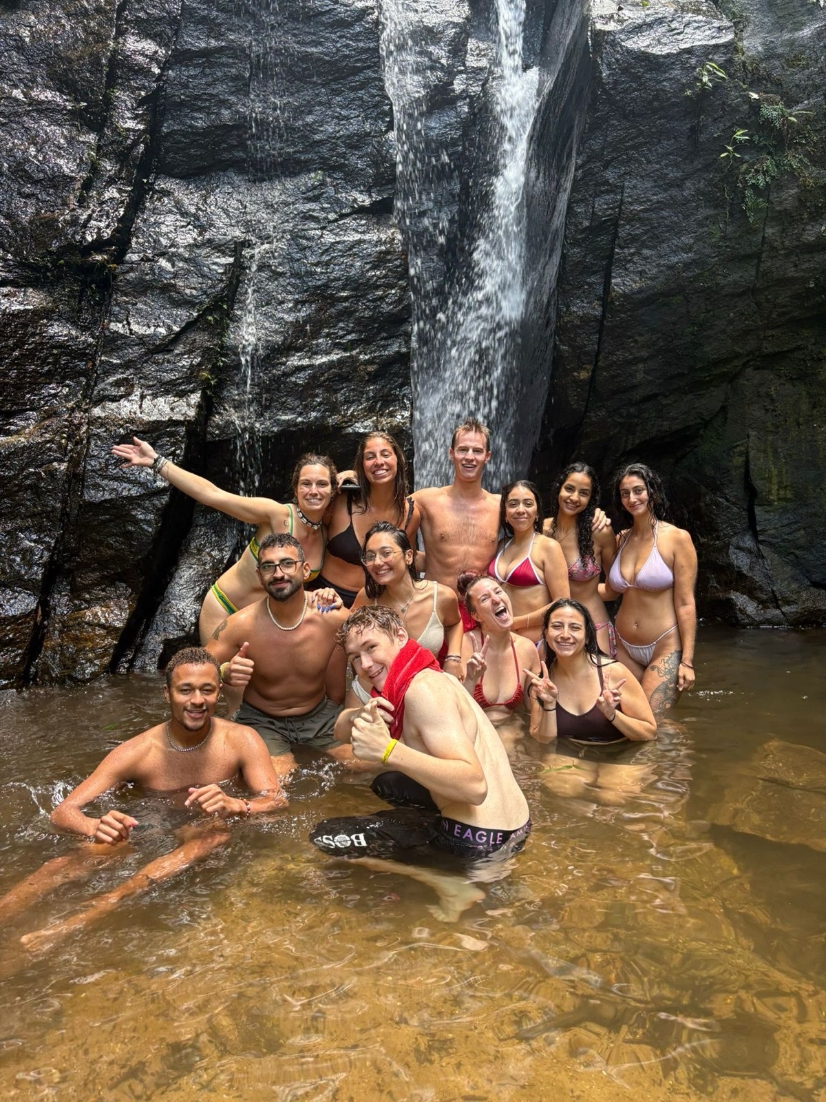 Volunteers standing together in a pool at the foot of a waterfall.