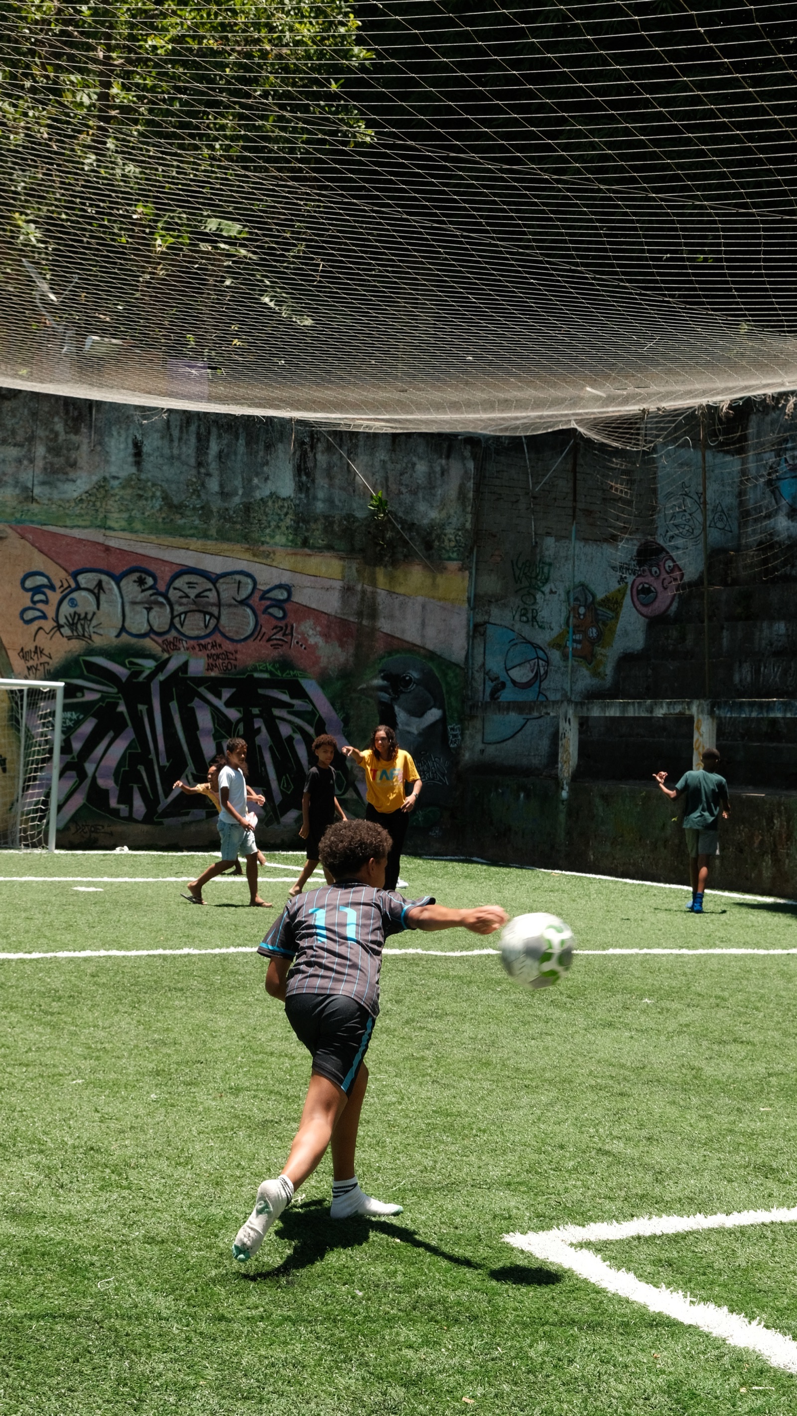 A boy kicks a football across the artificial pitch in Vidigal while other children play behind him.