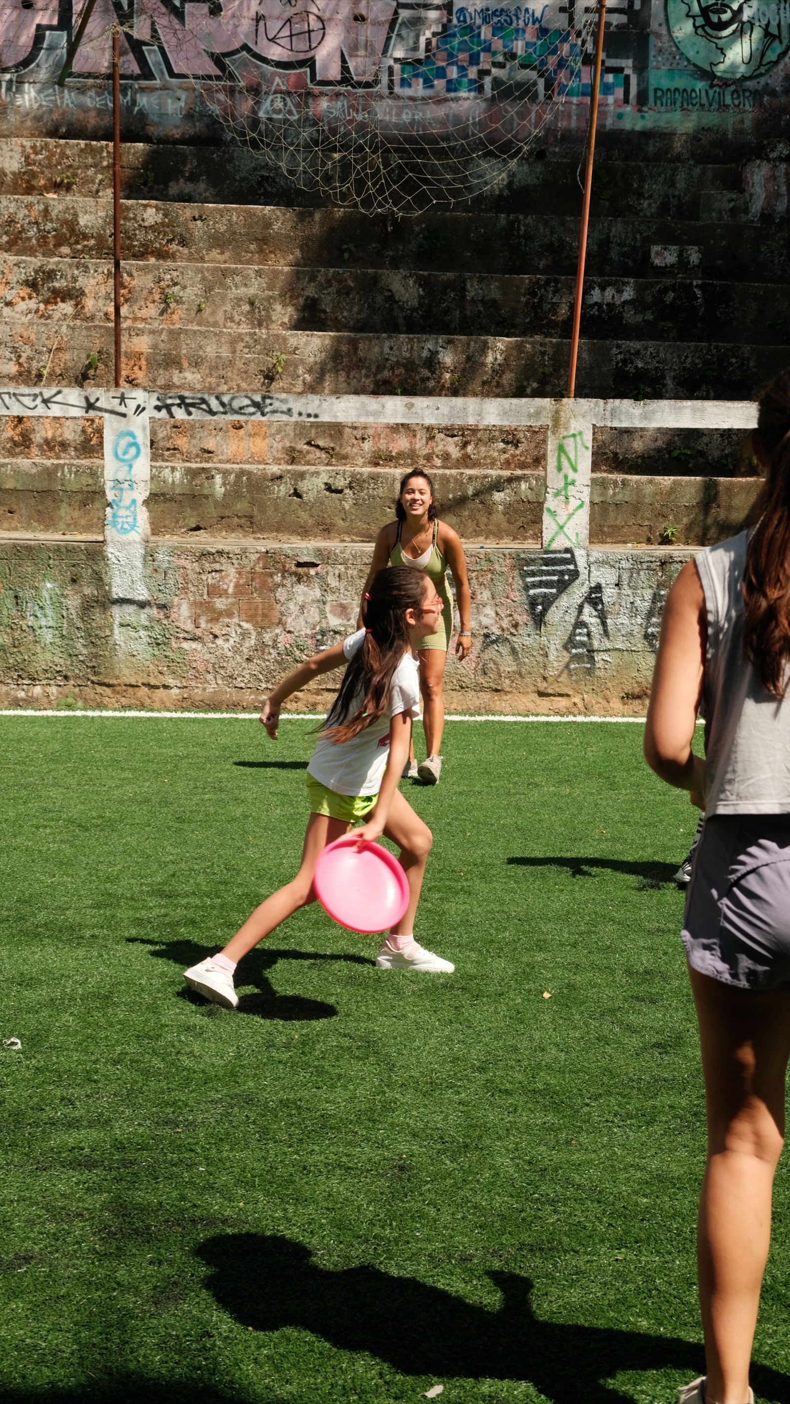 A girl runs with a pink frisbee across the pitch in Vidigal.