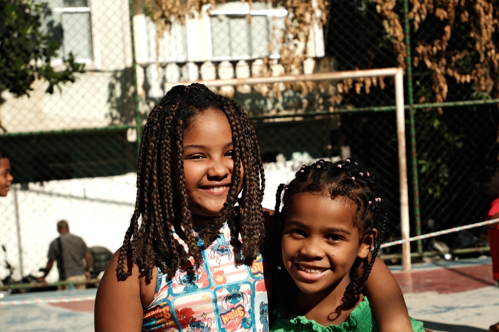 Two smiling girls with braided hair pose together close to the camera.